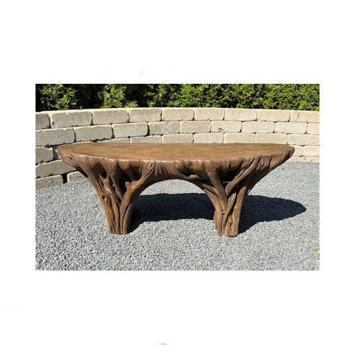 Wooden table with natural branch-like design on a stone surface with a stone wall and greenery in the background