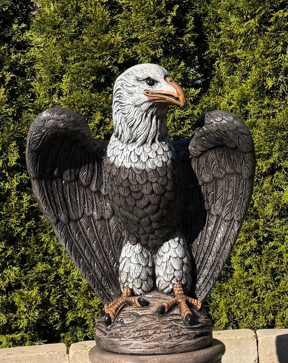 Statue of an eagle with outstretched wings against a green foliage background