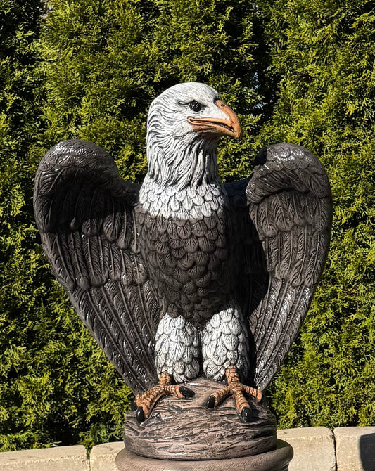 Statue of an eagle with outstretched wings against a green foliage background