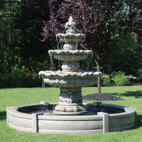 Three-tiered stone fountain in a garden setting with trees and grass.