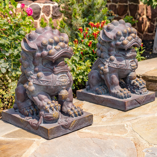 Two stone lion statues on a stone patio with garden flowers in the background