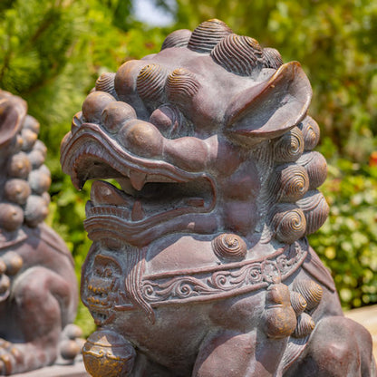 Bronze lion statue with detailed craftsmanship against a green foliage background close up of face