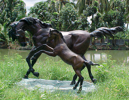 Bronze sculpture of a horse on grass with a pond and trees in the background