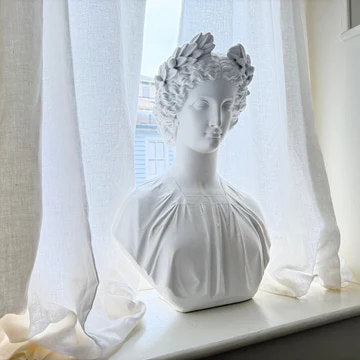 White classical bust Grecian Amazon woman on a windowsill with sheer curtains in the background