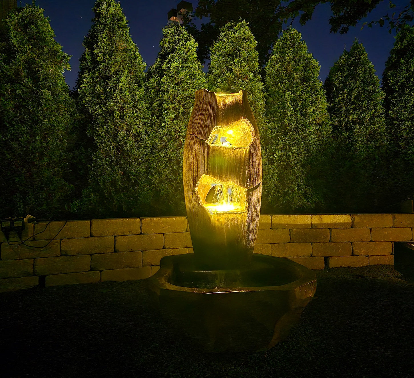 Illuminated grotto fountain with three cascading water levels  shown at night