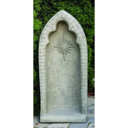 A freestanding arched stone garden wall feature or niche in light gray concrete, with a carved starburst motif in the center and a faux brick border, shown outdoors against green foliage and paving stones.