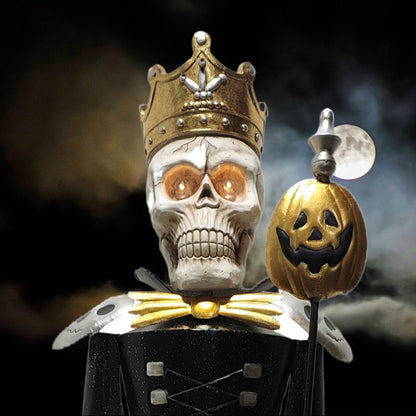 A Halloween decoration shaped like a skull wearing a gold crown and black-and-gold costume, holding a jack-o'-lantern staff against a dark smoky background with a moon visible.