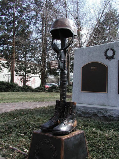 Statue of a helmet and boots on a pedestal with a plaque in the background