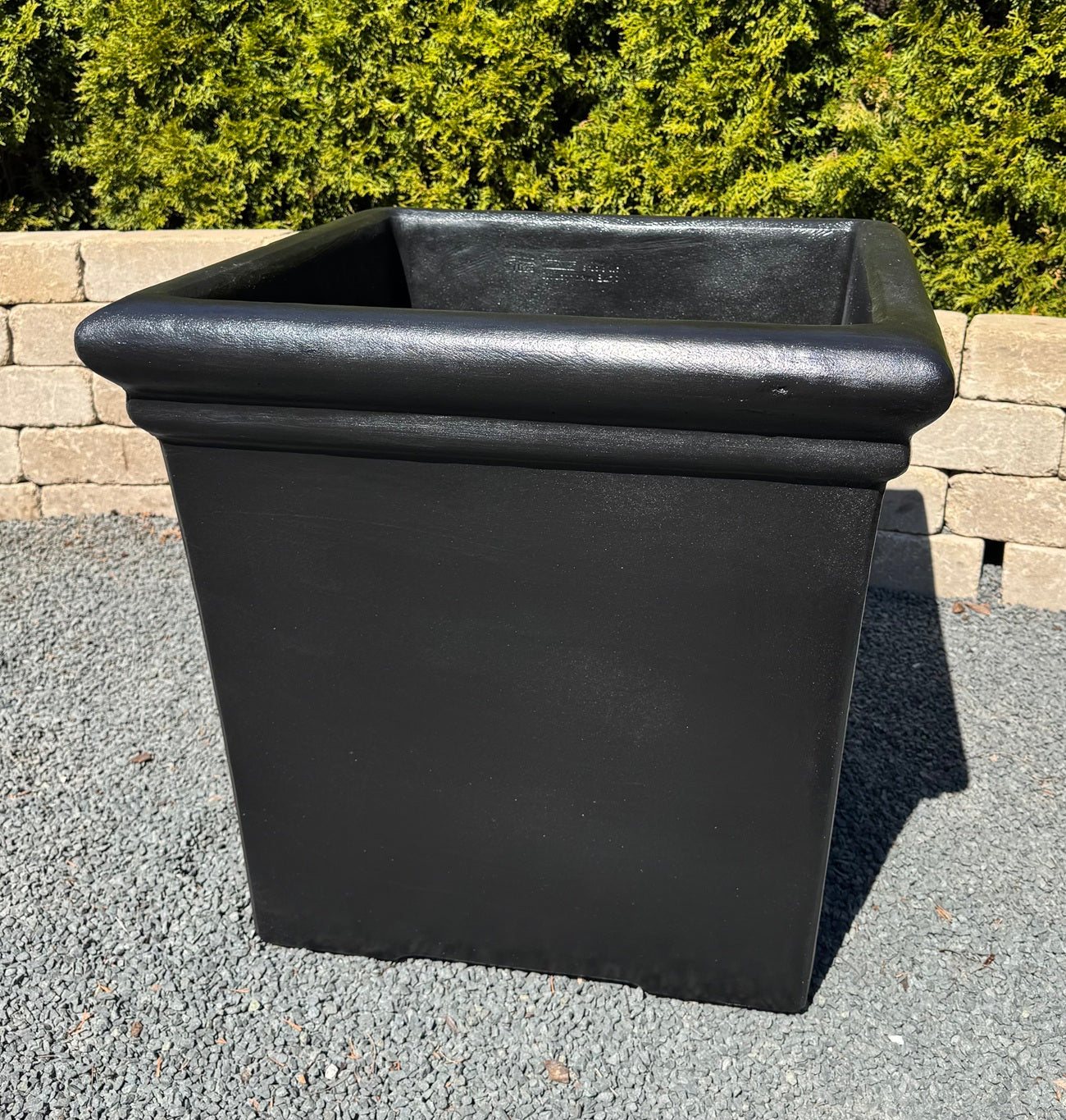 Black rectangular planter on a gravel surface with greenery in the background
