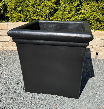 Black rectangular planter on a gravel surface with greenery in the background