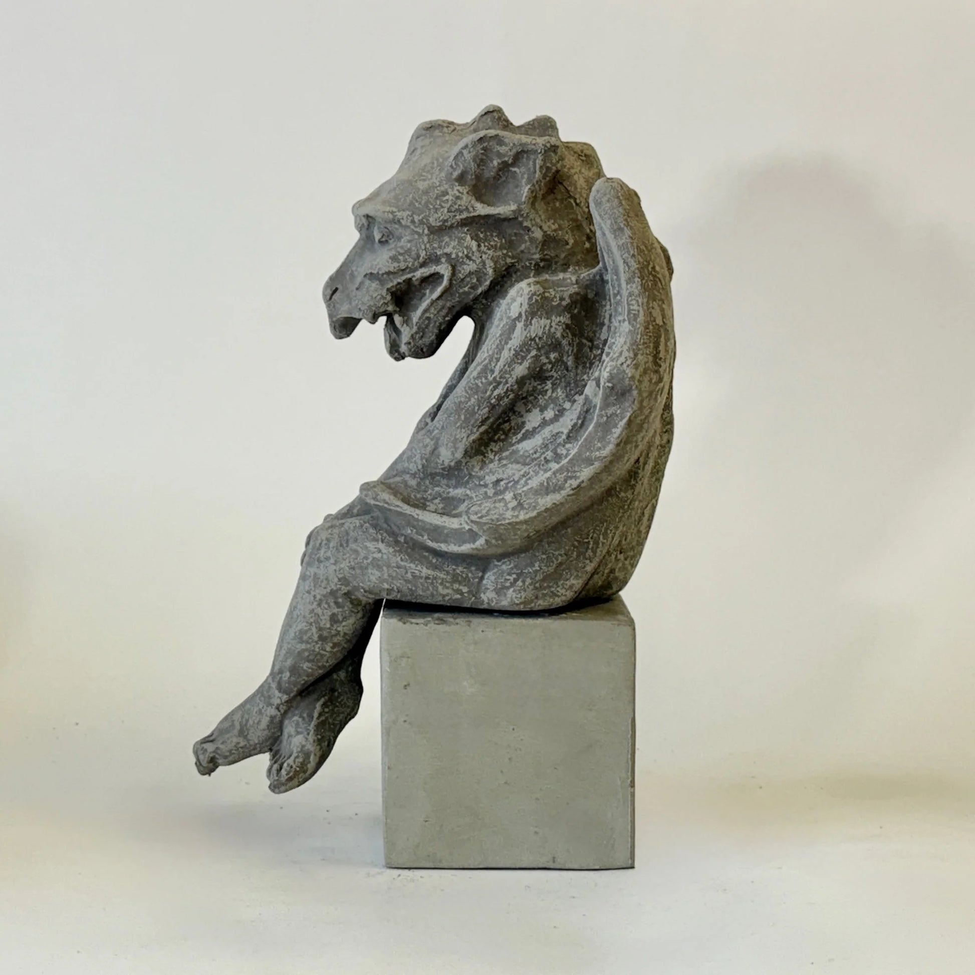 Stone gargoyle sculpture on a pedestal against a plain background