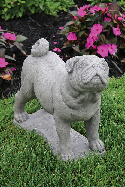Stone statue of a bulldog on grass with flowers in the background