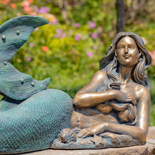 Bronze mermaid statue with fish tail in a garden setting