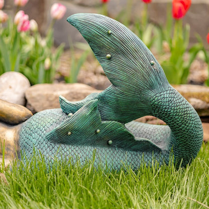Mermaid tail sculpture on grass with flowers in the background