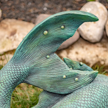 Close-up of a detailed green mermaid tail sculpture with pebbles and grass in the background.