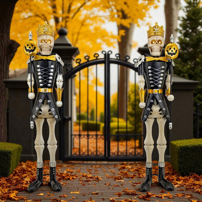 Two skeleton guards in Halloween costumes standing in front of a black gate with autumn leaves and trees in the background.
