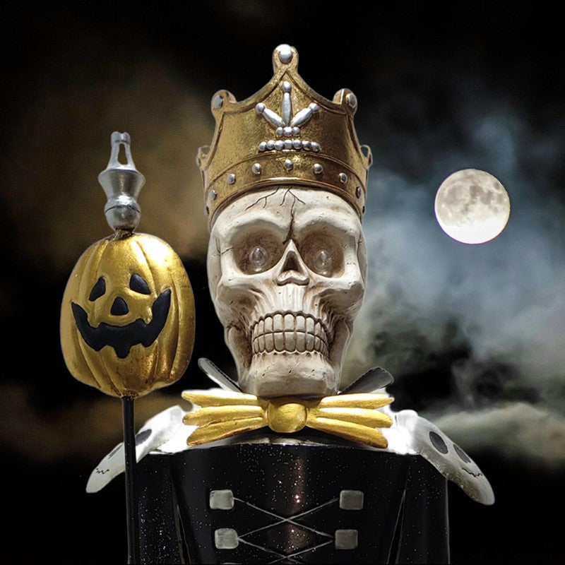 A decorative Halloween figurine of a crowned skull wearing a black and gold uniform, holding a jack-o'-lantern staff, set against a dark smoky night sky with a full moon.