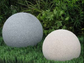 Two spherical garden statues, one gray and one off-white, placed on green grass with foliage in the background.