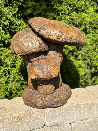 Rust-colored mushroom sculpture on a stone surface with green foliage in the background