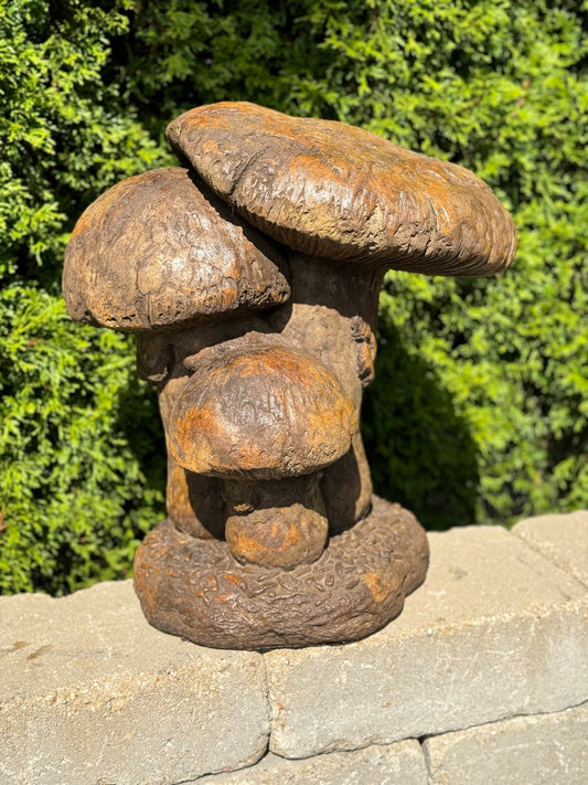 Rust-colored mushroom sculpture on a stone surface with green foliage in the background