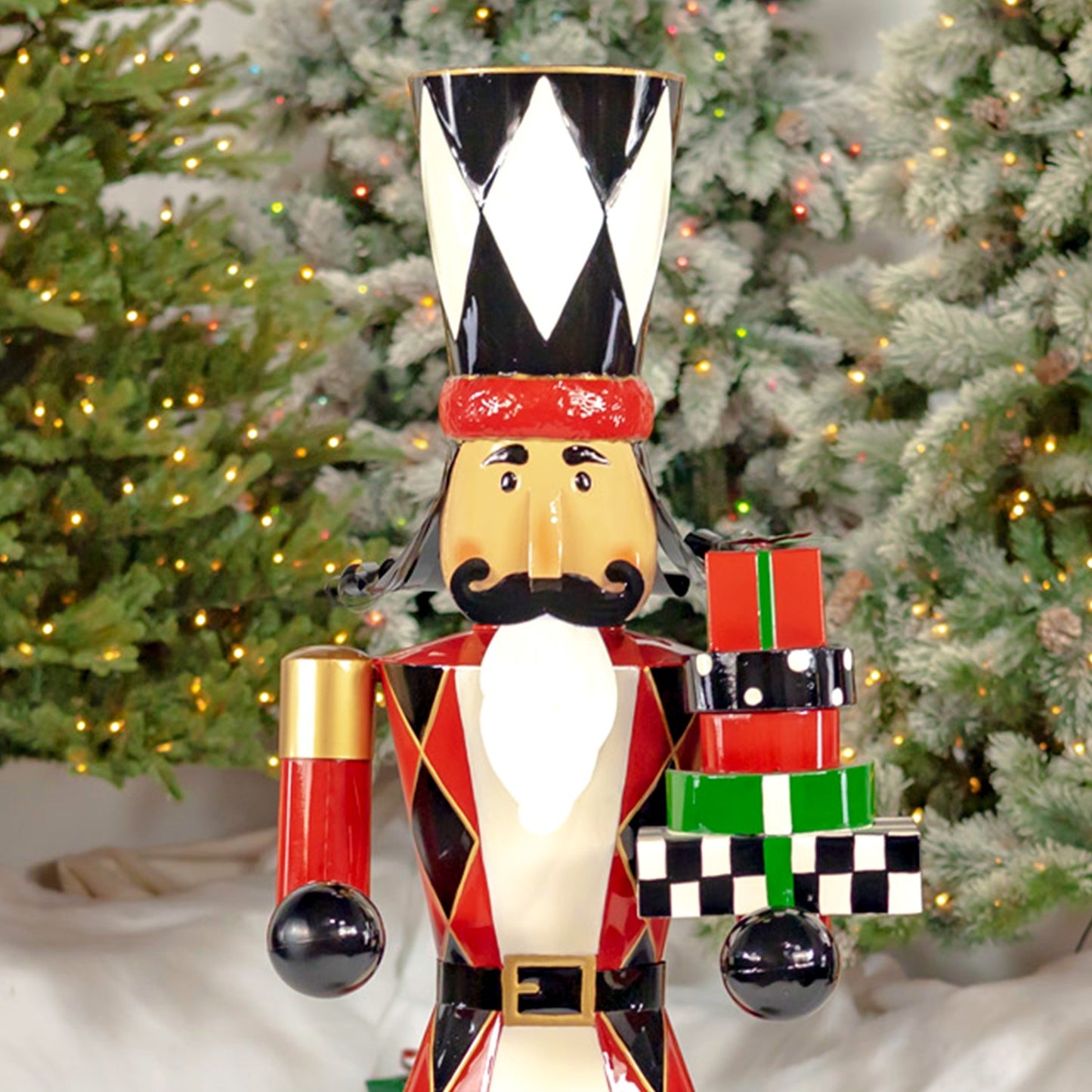Decorative nutcracker holding presents in front of a Christmas tree.