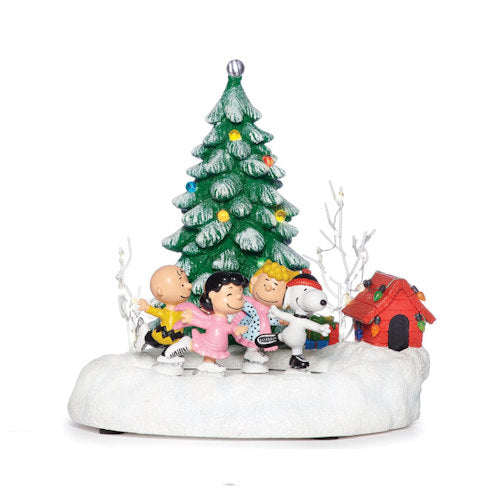 A festive Peanuts Christmas figurine featuring Charlie Brown, Snoopy, and other characters ice skating in front of a decorated green Christmas tree, set on a snowy white base with a red doghouse and white branches.