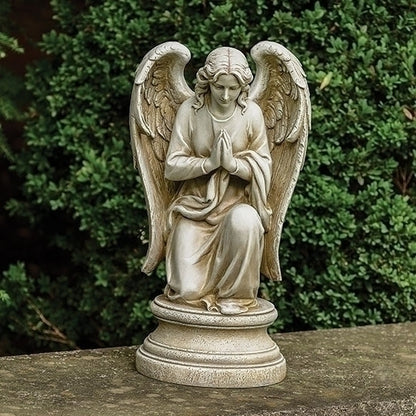 Statue of an angel with outstretched wings on a pedestal against a green foliage background