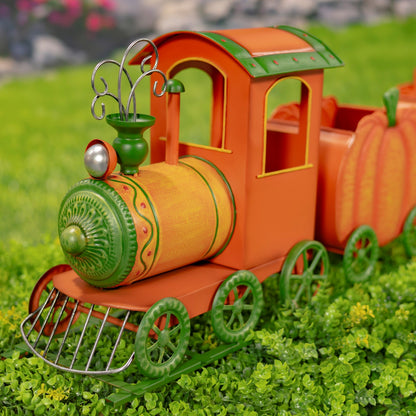 An orange and green metal decorative train toy shaped like a pumpkin, displayed on artificial green grass.