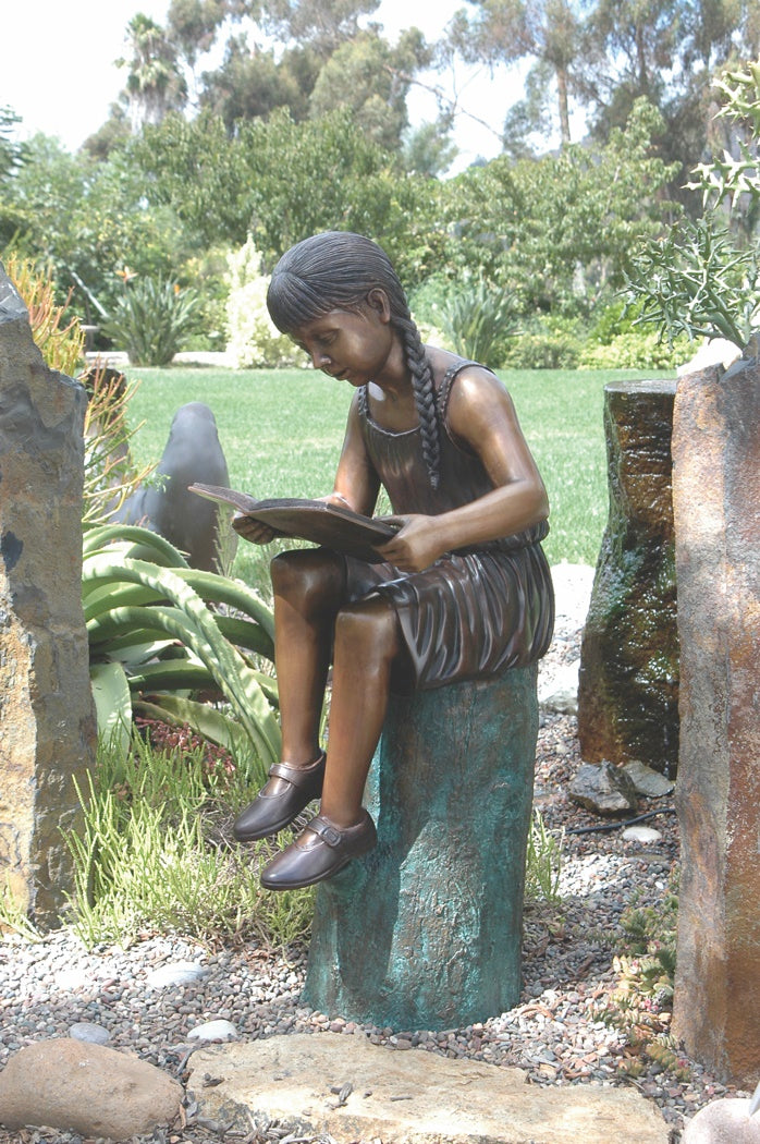 Girl with braided hair reading on log bronze sculpture