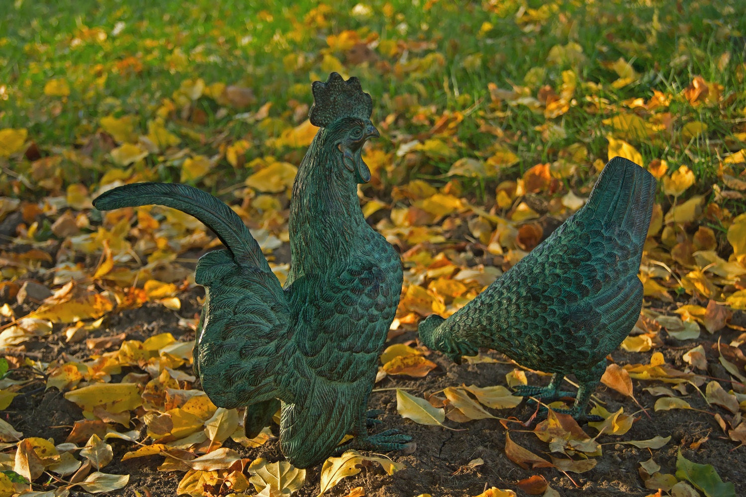 Verdigris hen and rooster sculptures among autumn leaves