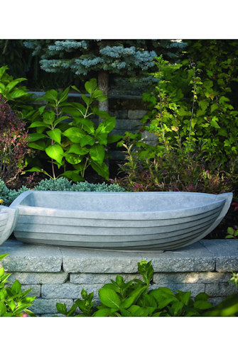 Decorative stone boat in a garden setting with greenery and a stone wall.