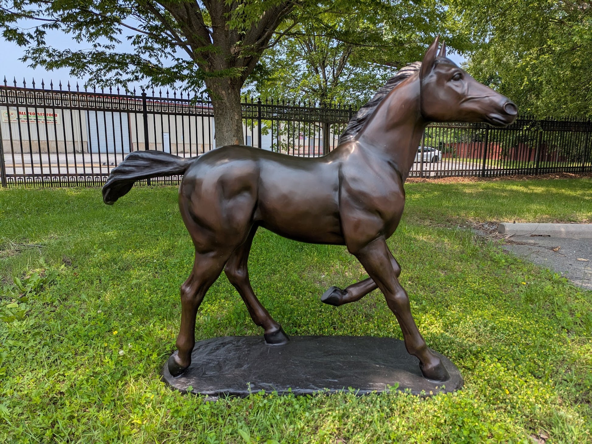 Bronze statue of a horse on grass with a fence and trees in the background
