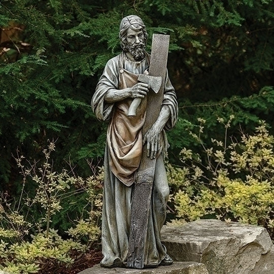 Saint Joseph the Worker Statue of a religious figure holding a axe and wood garden setting