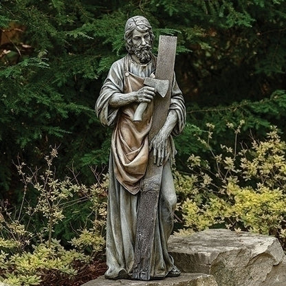 Saint Joseph the Worker Statue of a religious figure holding a axe and wood garden setting