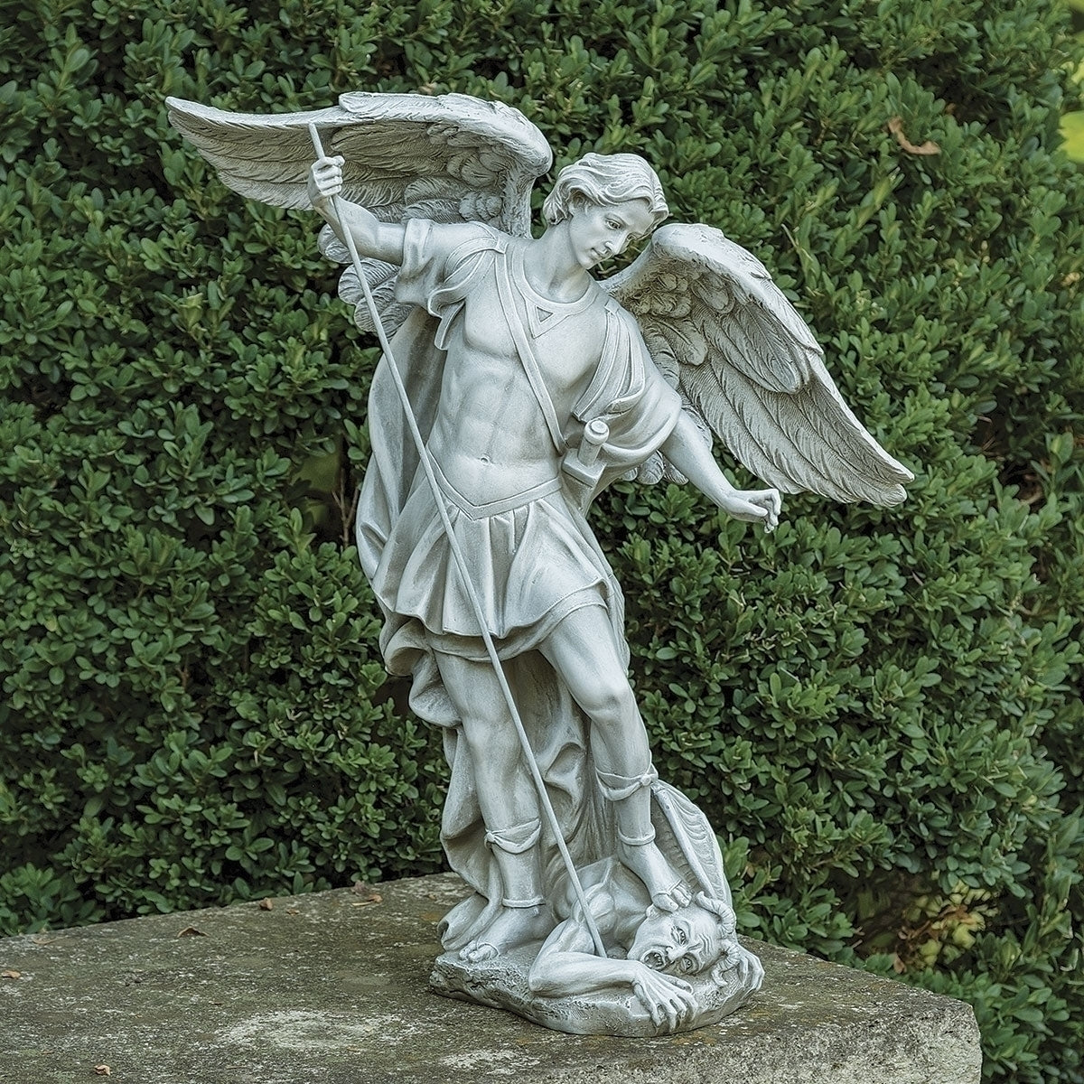 Saint Michael Garden Statue of an angel with a sword and shield against a green bush background