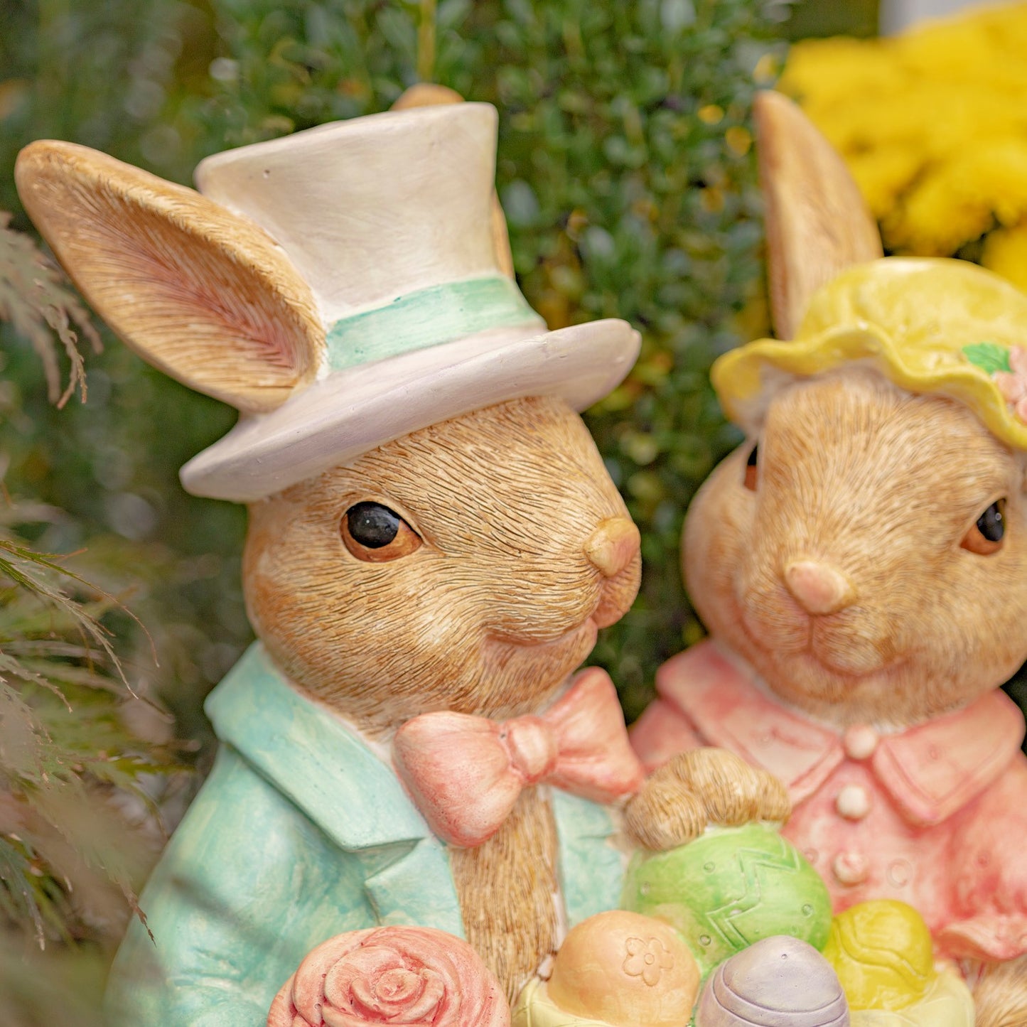 Two decorative rabbits wearing hats with Easter eggs and flowers.