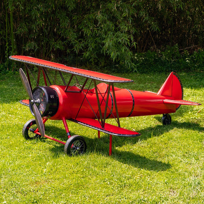 Red model airplane on grass with green foliage in the background