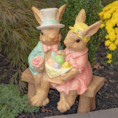 Decorative garden statues of a rabbit couple with an Easter basket, sitting on a bench.
