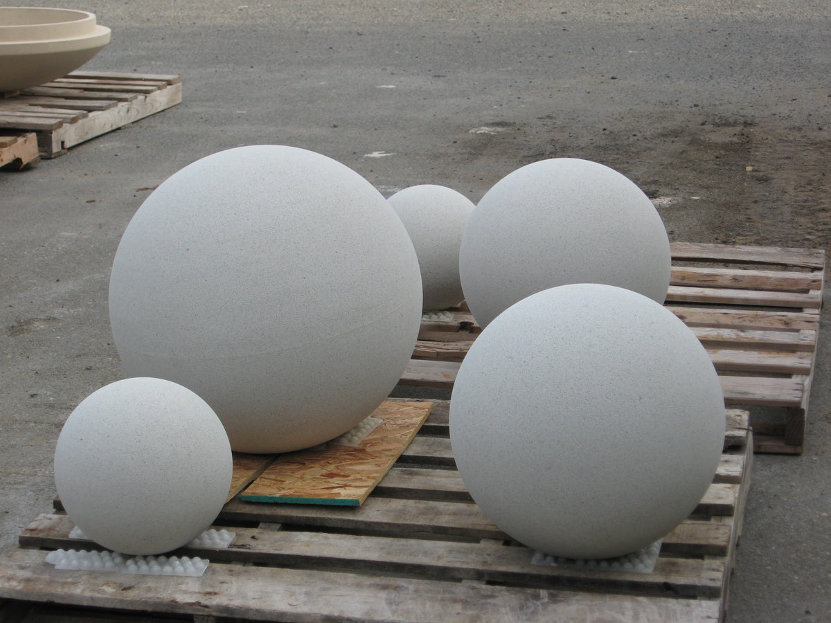 Five large white spherical stone or concrete plant markers of varying sizes displayed on wooden pallets outdoors on a gray concrete surface.