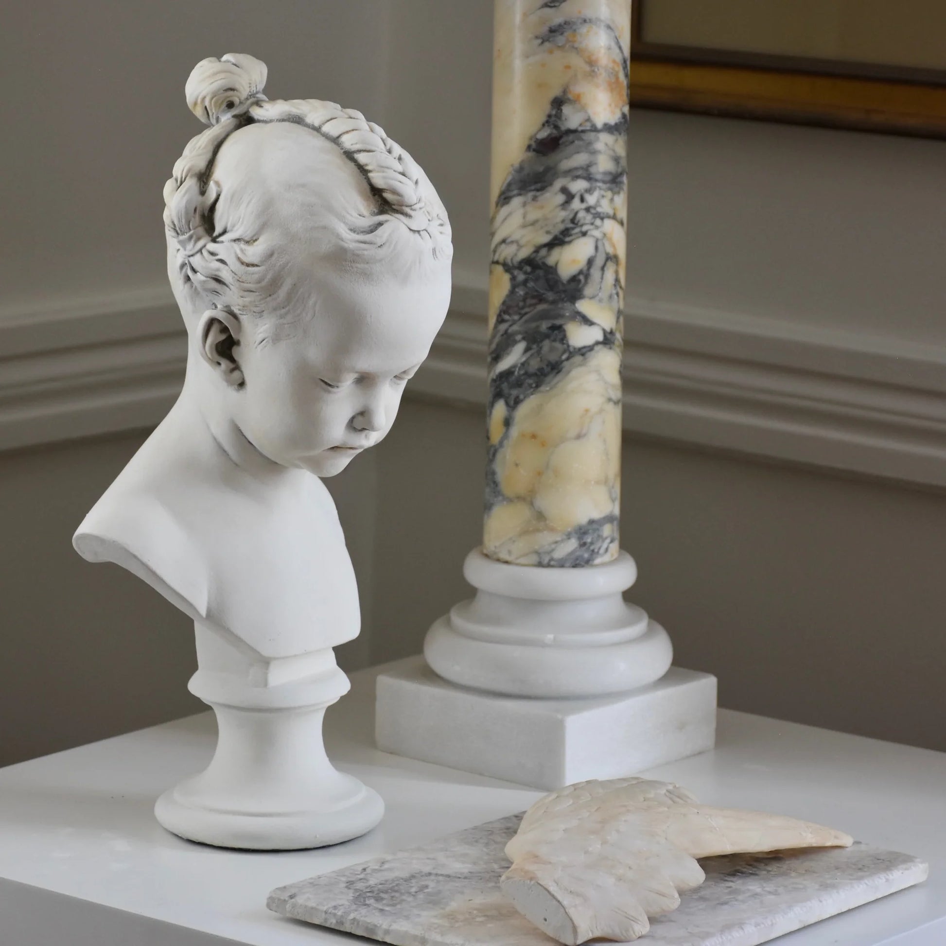 White marble bust of a child on a table with a marble column in the background