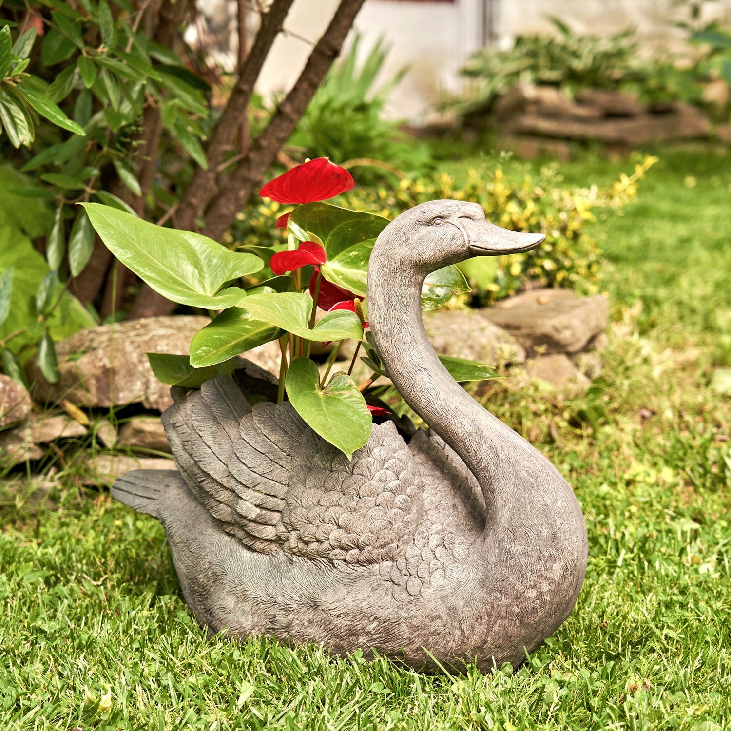 Gray swan-shaped planter with plants in a garden setting
