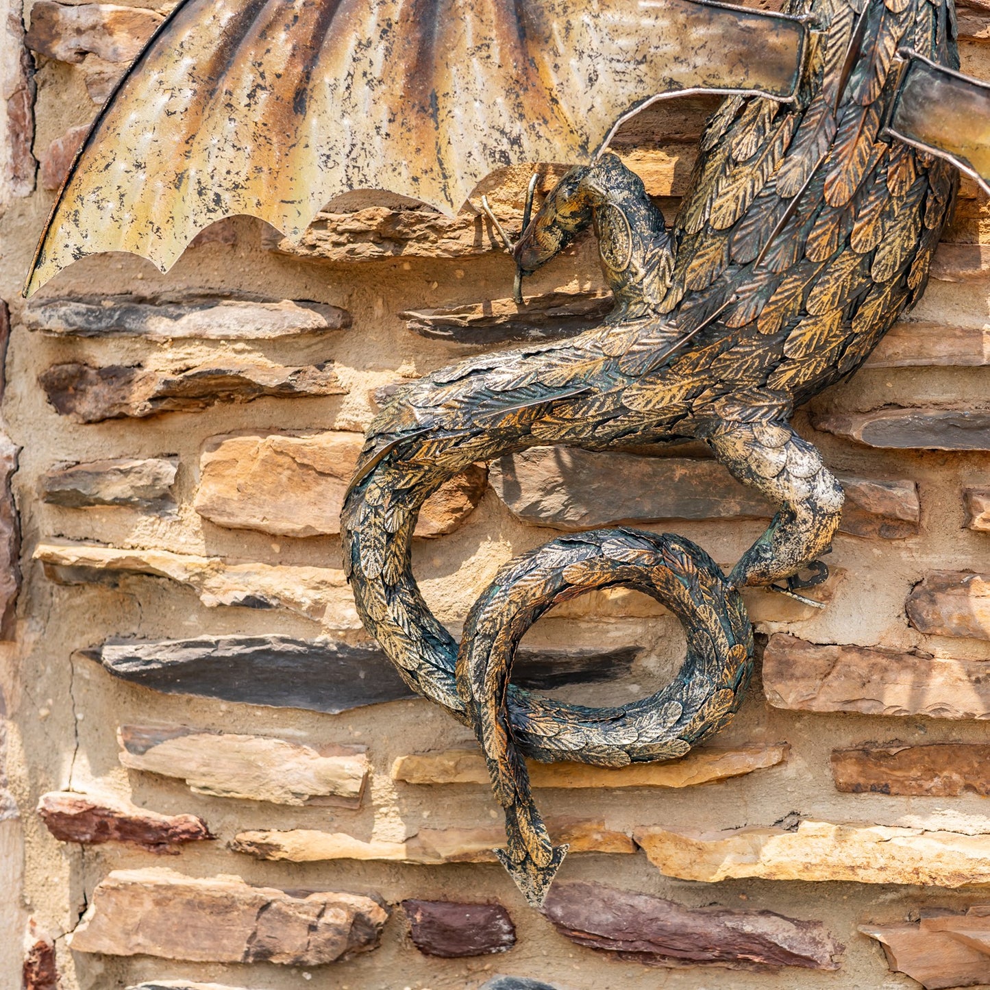 Tail close up Guardian Serpent wall dragon sculpture with coiled body and spread wings mounted on stone wall