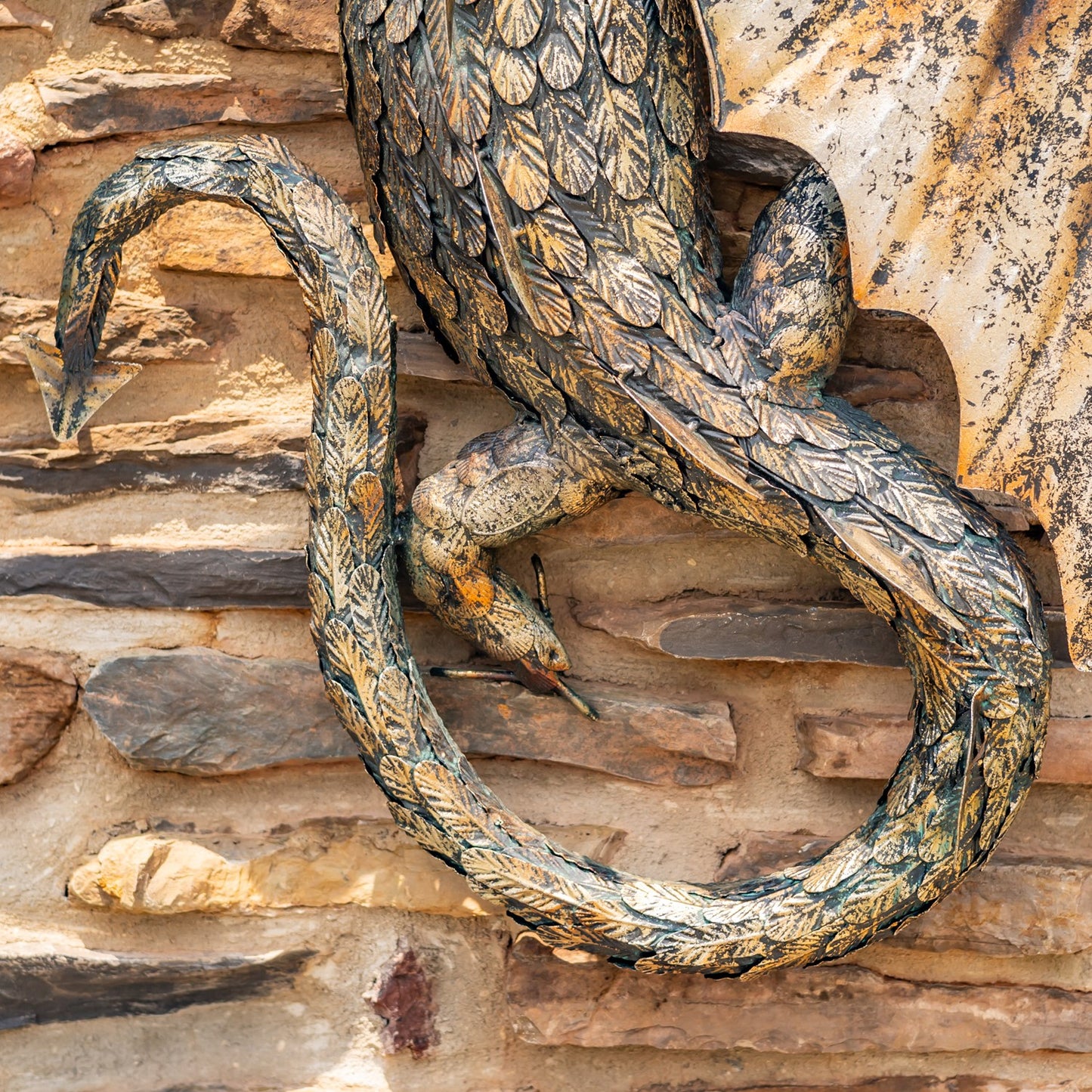 Tail view close up Guardian Serpent wall dragon sculpture with coiled body and spread wings mounted on stone wall