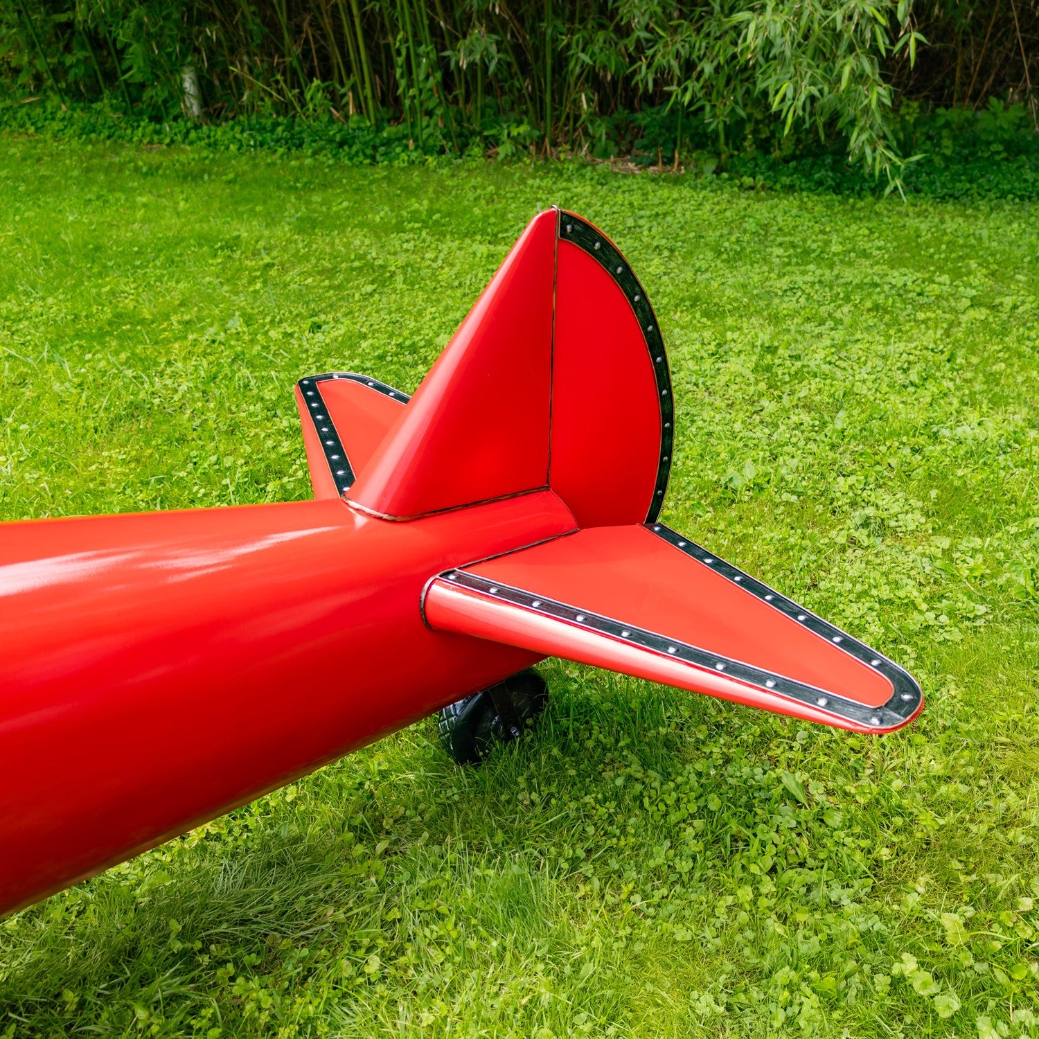 Close up of Tail Red airplane model on grass with green foliage in the background