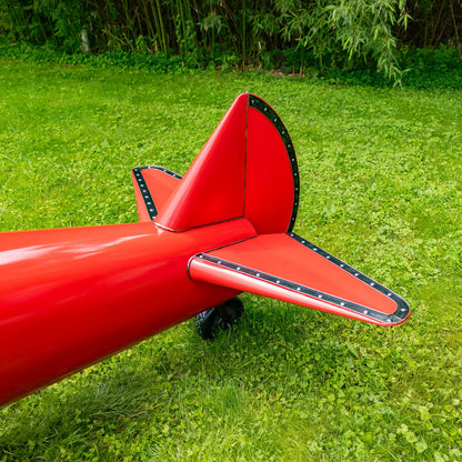 Close up of Tail Red airplane model on grass with green foliage in the background