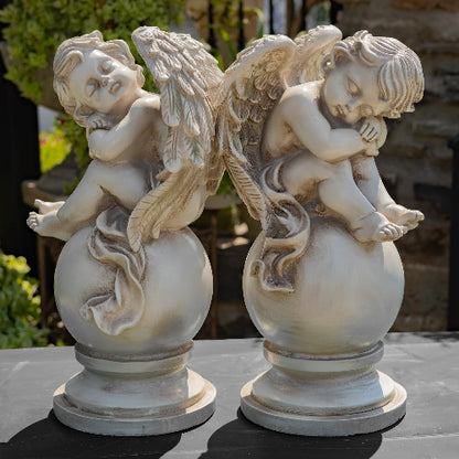 Two angel statues on spherical bases with a blurred garden background