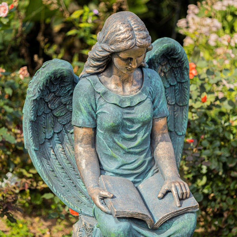 Statue of an angel reading a book in a garden setting