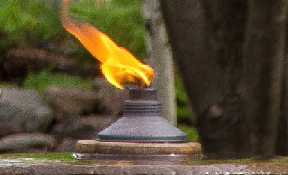 Flaming torch on a fountain top pedestal   shows fire when lit with a natural background