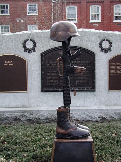 Memorial sculpture with helmet, boots, and rifle in front of a brick building with plaques.