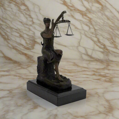 Blind lady justice, sitting down, with her hand waving above her scales of justice.  On a black marble base, with a white veined marble background.
